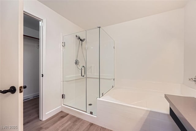 full bath featuring a spacious closet, a shower stall, a garden tub, and wood finished floors