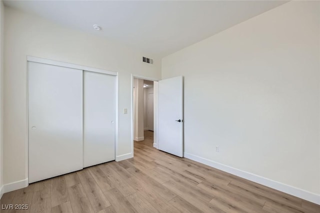 unfurnished bedroom featuring light wood-style flooring, baseboards, visible vents, and a closet