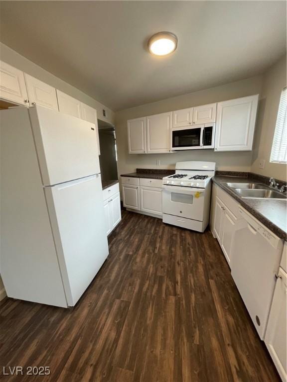 kitchen with dark wood finished floors, white appliances, dark countertops, and a sink