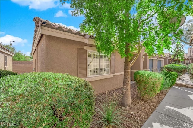 view of side of property featuring stucco siding, a tiled roof, and fence