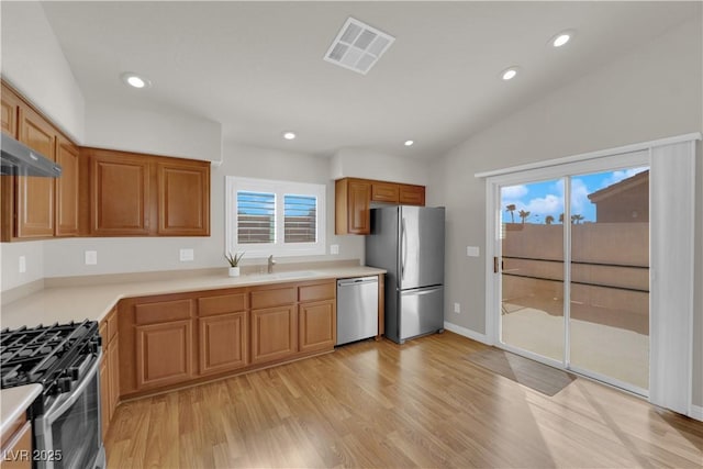 kitchen featuring visible vents, light wood-type flooring, vaulted ceiling, appliances with stainless steel finishes, and a sink