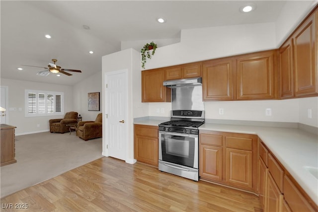 kitchen with stainless steel range with gas cooktop, lofted ceiling, recessed lighting, light countertops, and under cabinet range hood