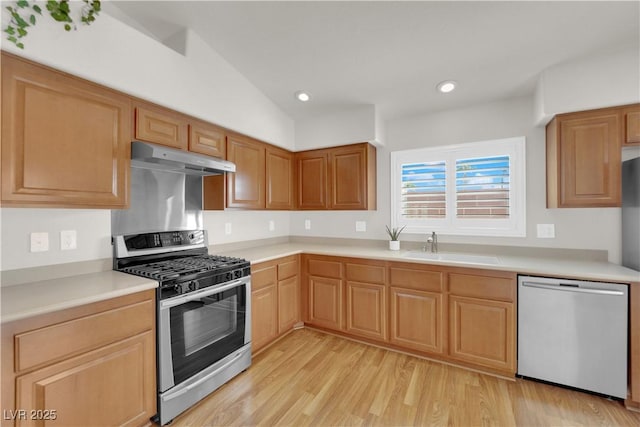 kitchen with a sink, stainless steel appliances, light countertops, under cabinet range hood, and light wood-type flooring