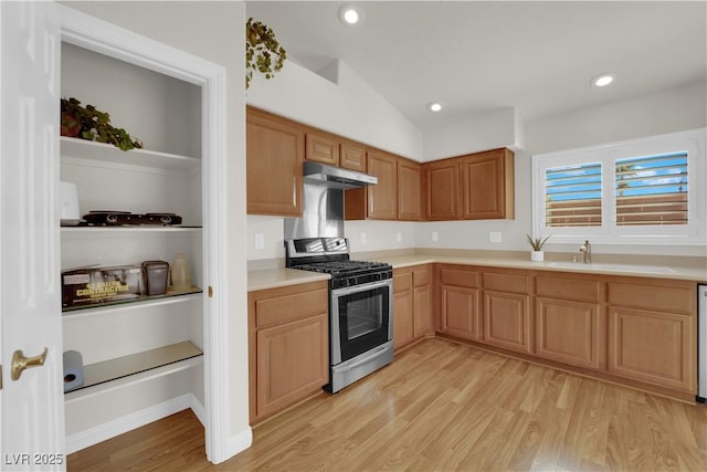 kitchen with stainless steel gas range oven, under cabinet range hood, light countertops, light wood-style floors, and a sink