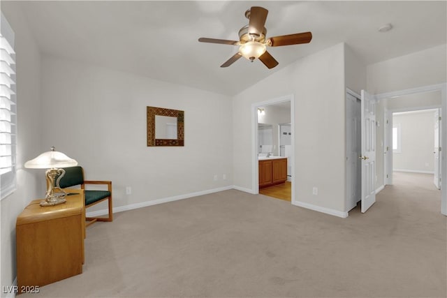 interior space featuring light carpet, a ceiling fan, ensuite bath, baseboards, and vaulted ceiling