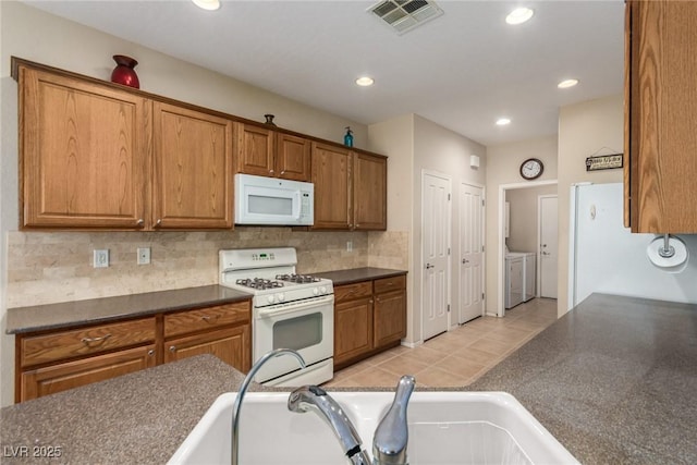 kitchen featuring white appliances, dark countertops, visible vents, and washer and clothes dryer