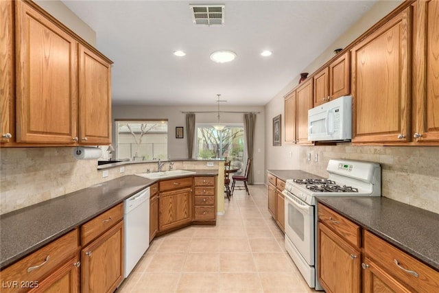 kitchen with dark countertops, white appliances, brown cabinetry, and a sink