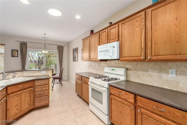 kitchen with dark countertops, light tile patterned floors, brown cabinetry, white appliances, and a sink