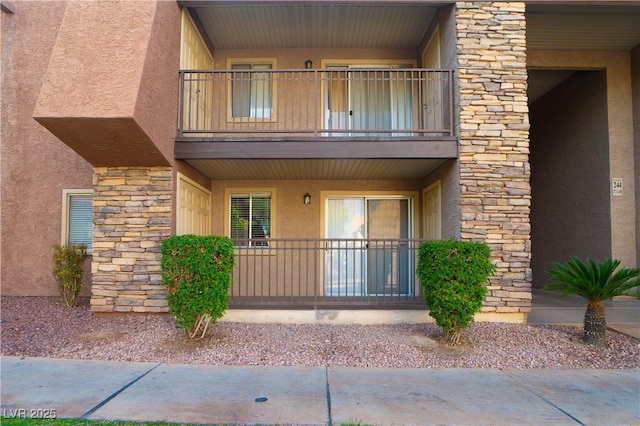 exterior space featuring stone siding, stucco siding, and a balcony