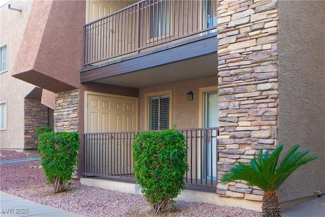 doorway to property featuring stone siding, stucco siding, and a balcony