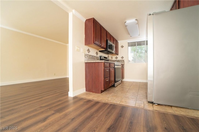 kitchen featuring ornamental molding, open floor plan, light wood-style floors, appliances with stainless steel finishes, and baseboards