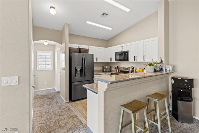 kitchen with visible vents, black appliances, a peninsula, a breakfast bar area, and white cabinets