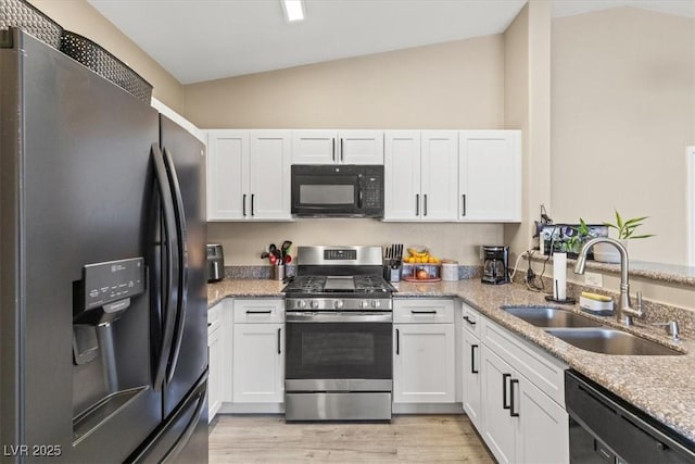 kitchen featuring light wood-type flooring, vaulted ceiling, light stone counters, black appliances, and a sink