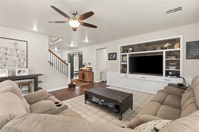 living area featuring stairway, baseboards, visible vents, ceiling fan, and a barn door