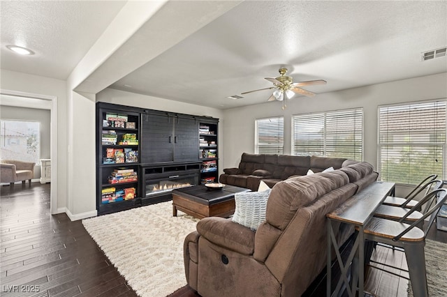 living area featuring a glass covered fireplace, visible vents, plenty of natural light, and dark wood finished floors