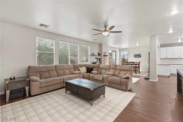 living room featuring a ceiling fan, baseboards, visible vents, and light wood finished floors