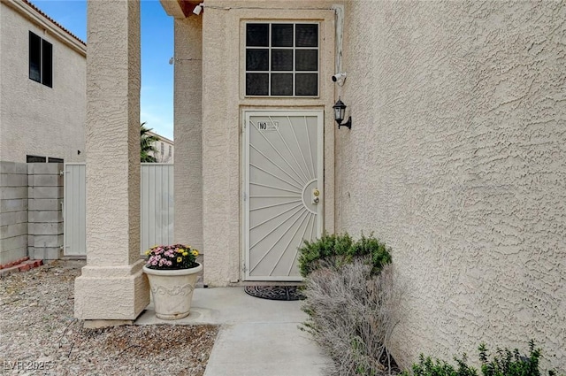 doorway to property featuring stucco siding and fence