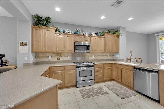 kitchen featuring visible vents, light brown cabinetry, a sink, stainless steel appliances, and a peninsula