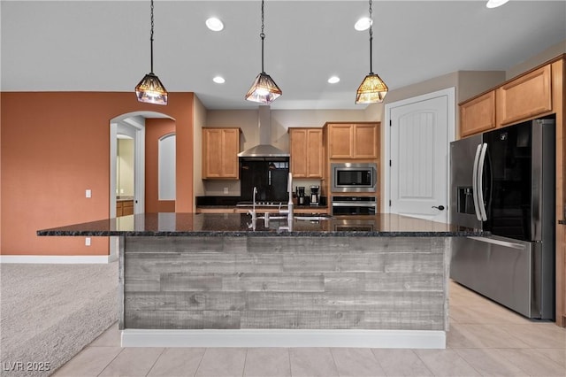 kitchen featuring a spacious island, wall chimney range hood, light tile patterned flooring, arched walkways, and stainless steel appliances