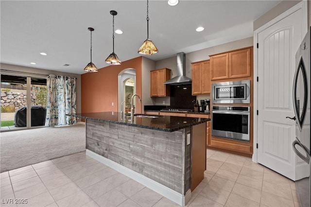 kitchen featuring dark stone counters, arched walkways, a sink, appliances with stainless steel finishes, and wall chimney range hood