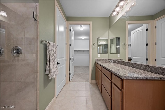 full bathroom with a walk in closet, baseboards, tiled shower, tile patterned floors, and vanity