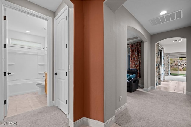 hallway with visible vents, arched walkways, carpet flooring, and tile patterned flooring