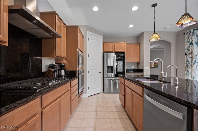 kitchen with dark stone countertops, a sink, stainless steel appliances, pendant lighting, and wall chimney exhaust hood