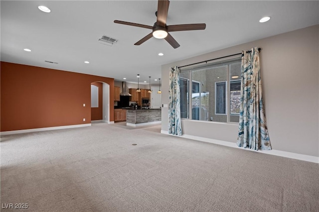 unfurnished living room with arched walkways, light colored carpet, and baseboards