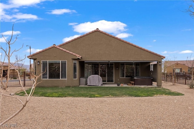 rear view of house featuring stucco siding, a tile roof, a hot tub, a fenced backyard, and a patio area