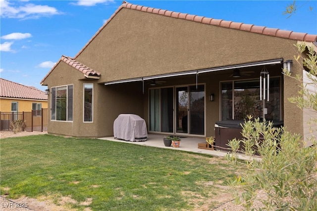 rear view of property with a lawn, a ceiling fan, fence, a patio area, and a hot tub