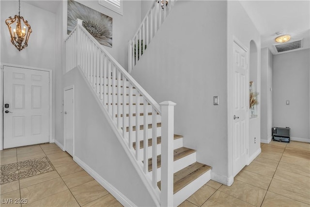 staircase featuring baseboards, visible vents, an inviting chandelier, a high ceiling, and tile patterned flooring