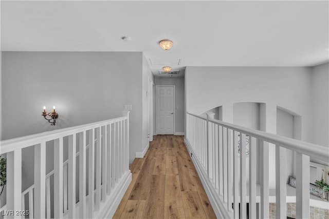 corridor featuring attic access, light wood-style flooring, an upstairs landing, and baseboards