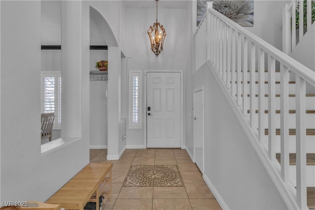 tiled entryway with stairs, a high ceiling, a notable chandelier, and baseboards