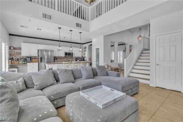 living room featuring stairs, light tile patterned flooring, arched walkways, and visible vents