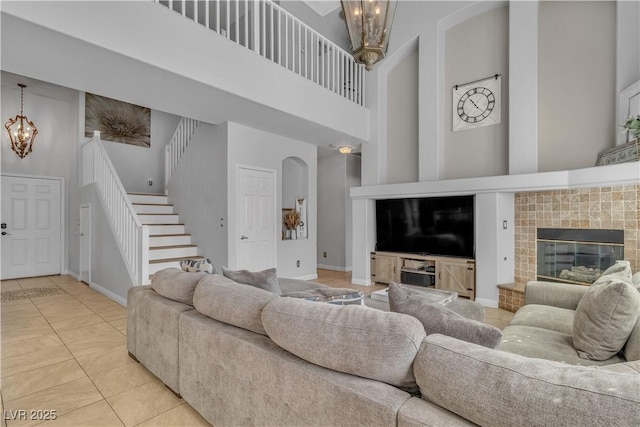 living area featuring stairway, a notable chandelier, a fireplace, and a high ceiling