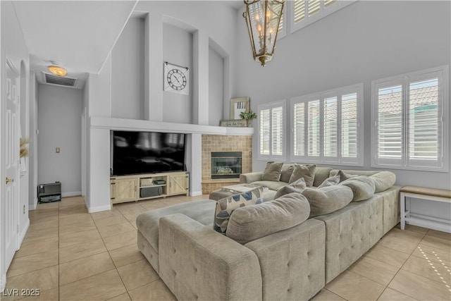 living area with visible vents, baseboards, light tile patterned floors, a towering ceiling, and a glass covered fireplace