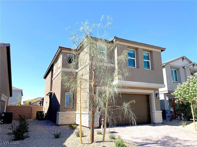 view of front of house with fence, stucco siding, decorative driveway, a garage, and stone siding