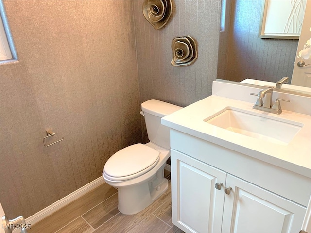 bathroom featuring toilet, vanity, baseboards, and wood tiled floor