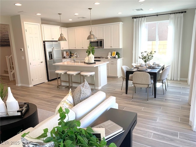 kitchen with wood finish floors, visible vents, a kitchen island with sink, stainless steel appliances, and light countertops