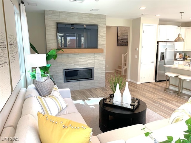 living area with a tiled fireplace, stairway, baseboards, and wood tiled floor