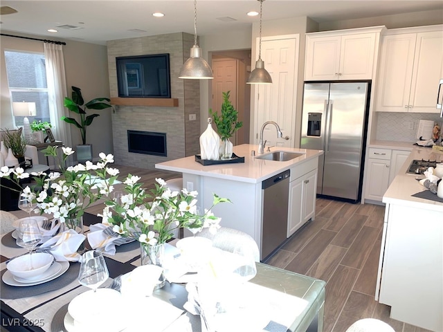 kitchen featuring wood finish floors, a sink, light countertops, appliances with stainless steel finishes, and a large fireplace