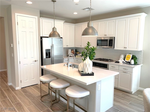 kitchen featuring visible vents, wood tiled floor, decorative backsplash, stainless steel appliances, and a sink