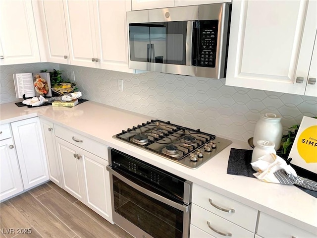 kitchen featuring stainless steel appliances, backsplash, light countertops, and white cabinetry