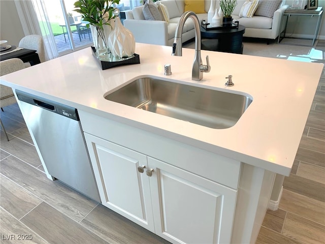 kitchen with wood finish floors, dishwasher, light countertops, white cabinetry, and a sink