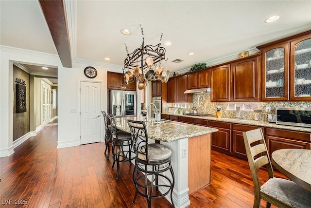 kitchen with dark wood finished floors, a breakfast bar area, under cabinet range hood, and stainless steel appliances