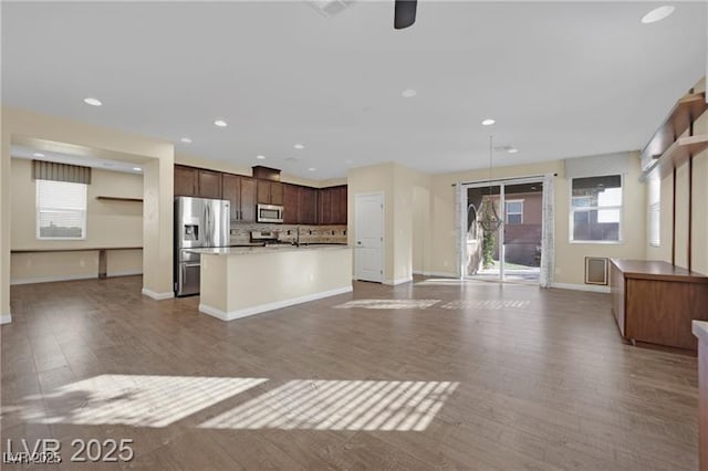 kitchen featuring dark wood finished floors, a kitchen island with sink, decorative backsplash, appliances with stainless steel finishes, and open floor plan