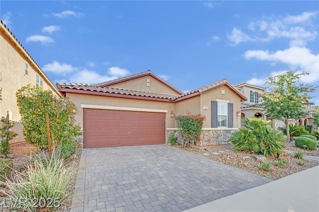 mediterranean / spanish home featuring stucco siding, a garage, stone siding, a tile roof, and decorative driveway