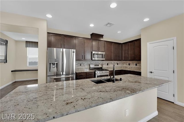 kitchen featuring visible vents, dark brown cabinets, light stone counters, decorative backsplash, and stainless steel appliances