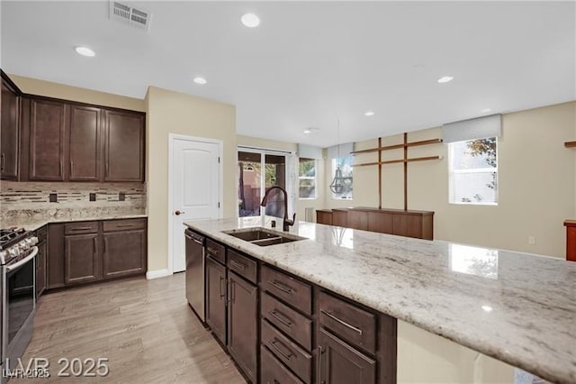 kitchen featuring light stone counters, visible vents, light wood-style flooring, stainless steel appliances, and a sink