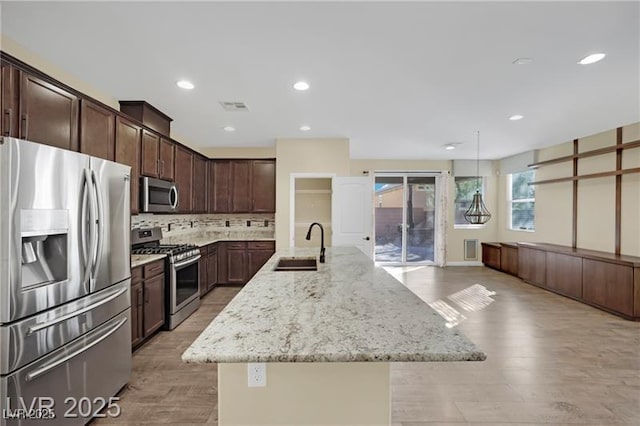 kitchen featuring visible vents, dark brown cabinetry, light stone counters, appliances with stainless steel finishes, and a sink